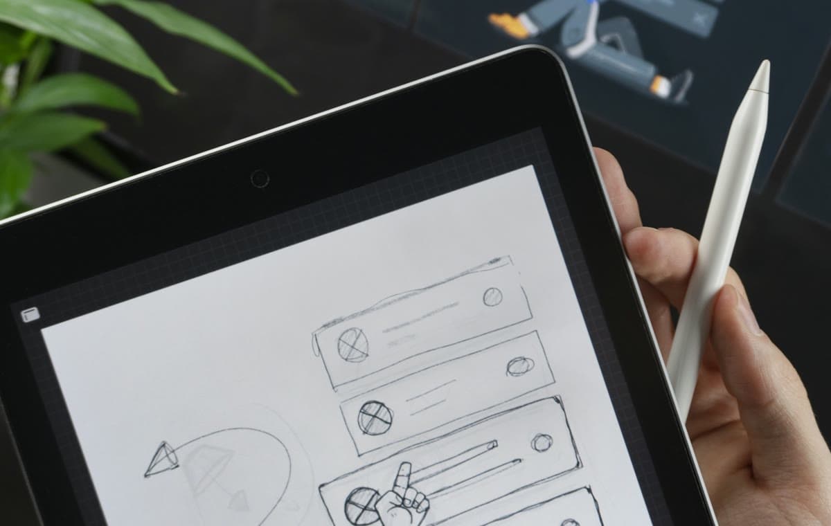 線画が表示されたタブレットのそばで白いスタイラスを持つ手と背景のモニター