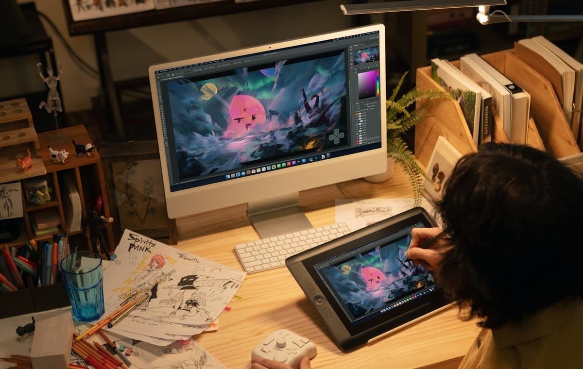 制作資料を並べた机で、ペンタブレットを使いデジタルイラストを描く人物