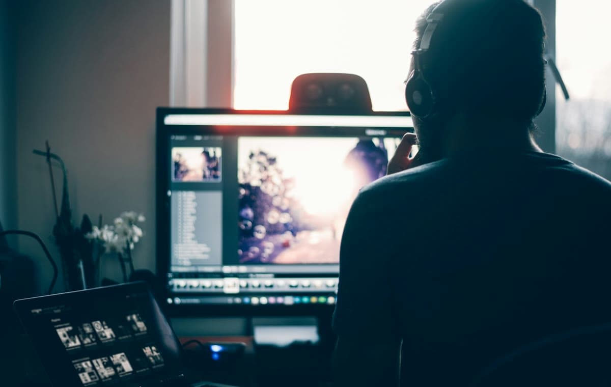 ヘッドホンを着けた人物がデスクトップ画面で写真を編集している後ろ姿