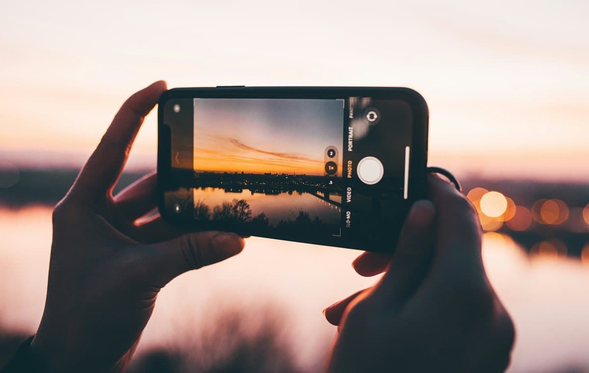夕暮れの空と川をスマートフォンのカメラ画面に収めようとしている両手