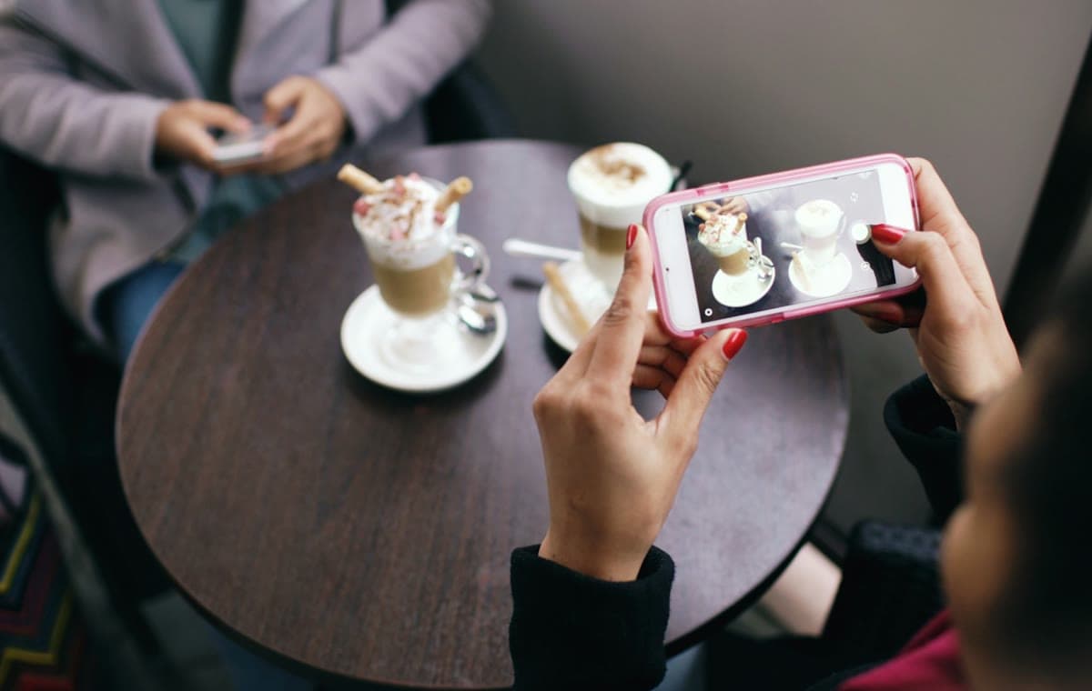 カフェのテーブルでコーヒードリンクをスマートフォンで撮影する女性の手元